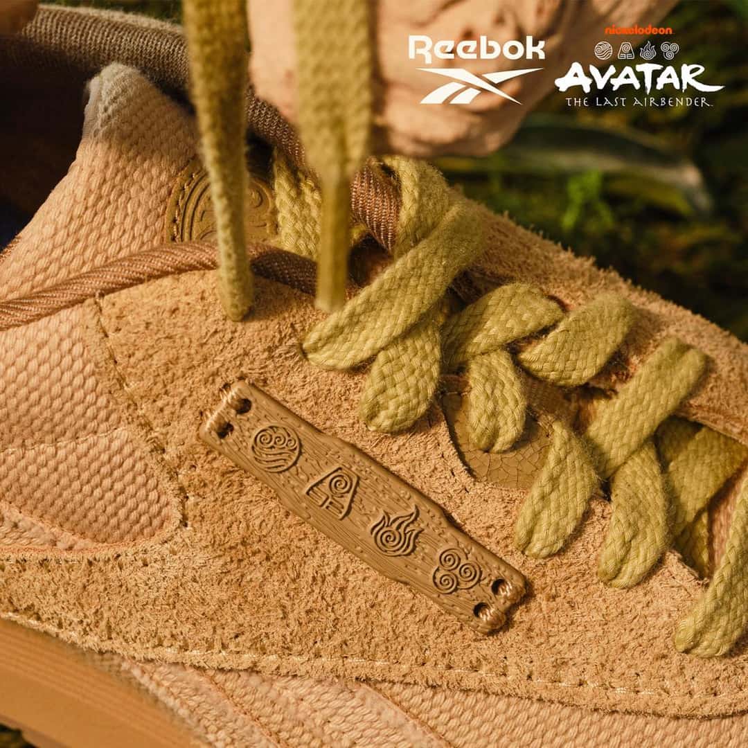 Detalle de la Reebok Classic Nylon Avatar en gamuza tostada, con una placa marrón que muestra los símbolos de las cuatro naciones y cordones gruesos verde oliva