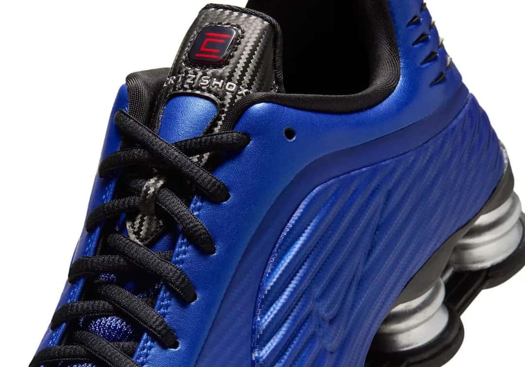 Detalle del Corteiz x Nike Shox R419 Mystique, con la textura tipo fibra de carbono en el talón, la etiqueta Shox en la lengüeta y los relieves azules del costado