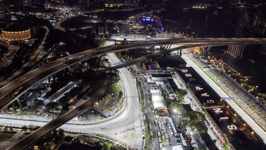 Vista aérea nocturna del circuito callejero de Marina Bay, con la recta de boxes iluminada, las tribunas llenas y las autopistas que pasan por encima del trazado