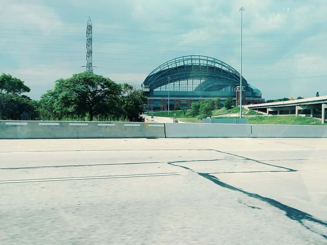 Imagen del estadio: el American Family Field visto desde la autopista, con su techo de arcos y un cielo nublado