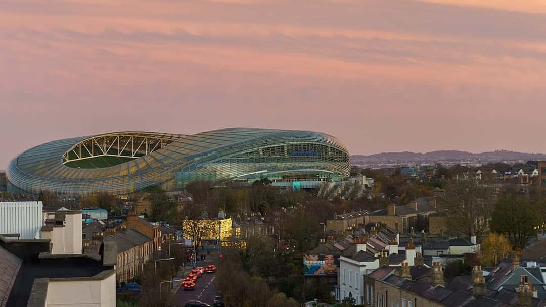 El Aviva Stadium de Dublín, con su techo de vidrio iluminado, al atardecer y rodeado de casas del barrio