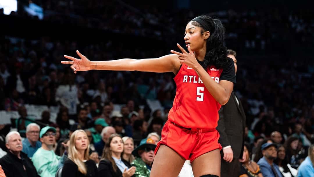 Angel Reese, con la camiseta roja número 5 de Atlanta Dream, hace un gesto con las dos manos frente a la tribuna durante el tercer partido de la semifinal en Nueva York