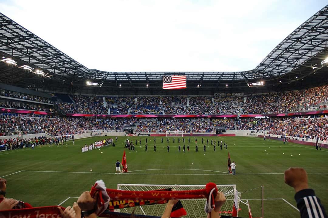 El estadio de los New York Red Bulls en Harrison, Nueva Jersey, visto desde atrás de un arco, con las tribunas llenas y la bandera de Estados Unidos en el techo; foto de archivo de 2010 (foto: Sam Szapucki, Wikimedia Commons, licencia CC BY 2.0)