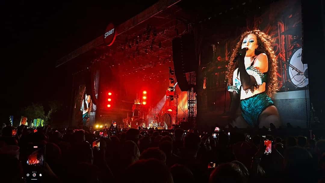 Foto de archivo de Chappell Roan en el festival Sziget de Budapest, en agosto de 2025: la cantante, con rulos colorados y maquillaje turquesa, aparece en una pantalla gigante junto al escenario iluminado de rojo, frente a una multitud con celulares en alto. Foto: GYSZ, Wikimedia Commons, CC BY-SA 4.0