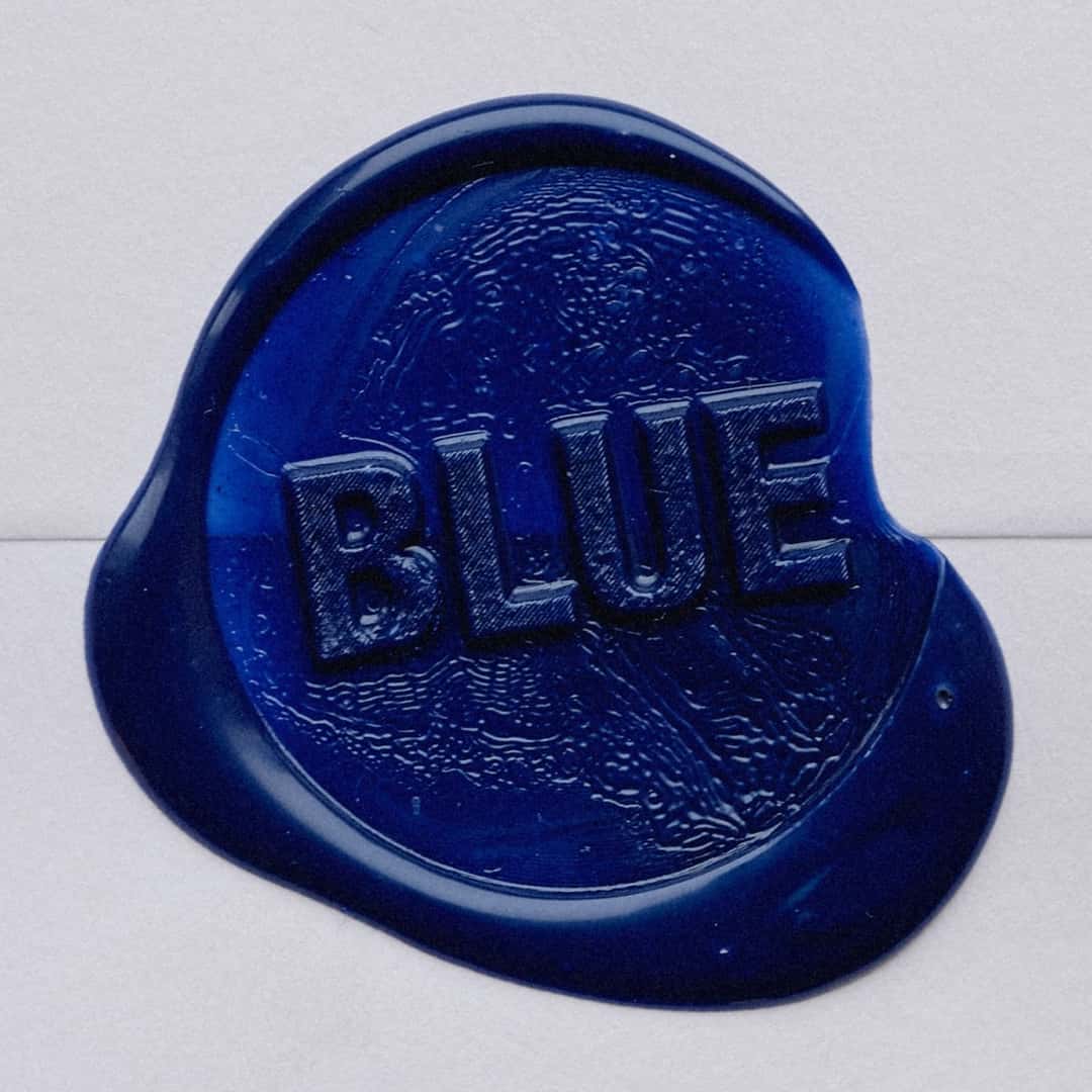 Portada de «BLUE»: un sello de lacre azul oscuro con la palabra «BLUE» en relieve, sobre un fondo gris claro