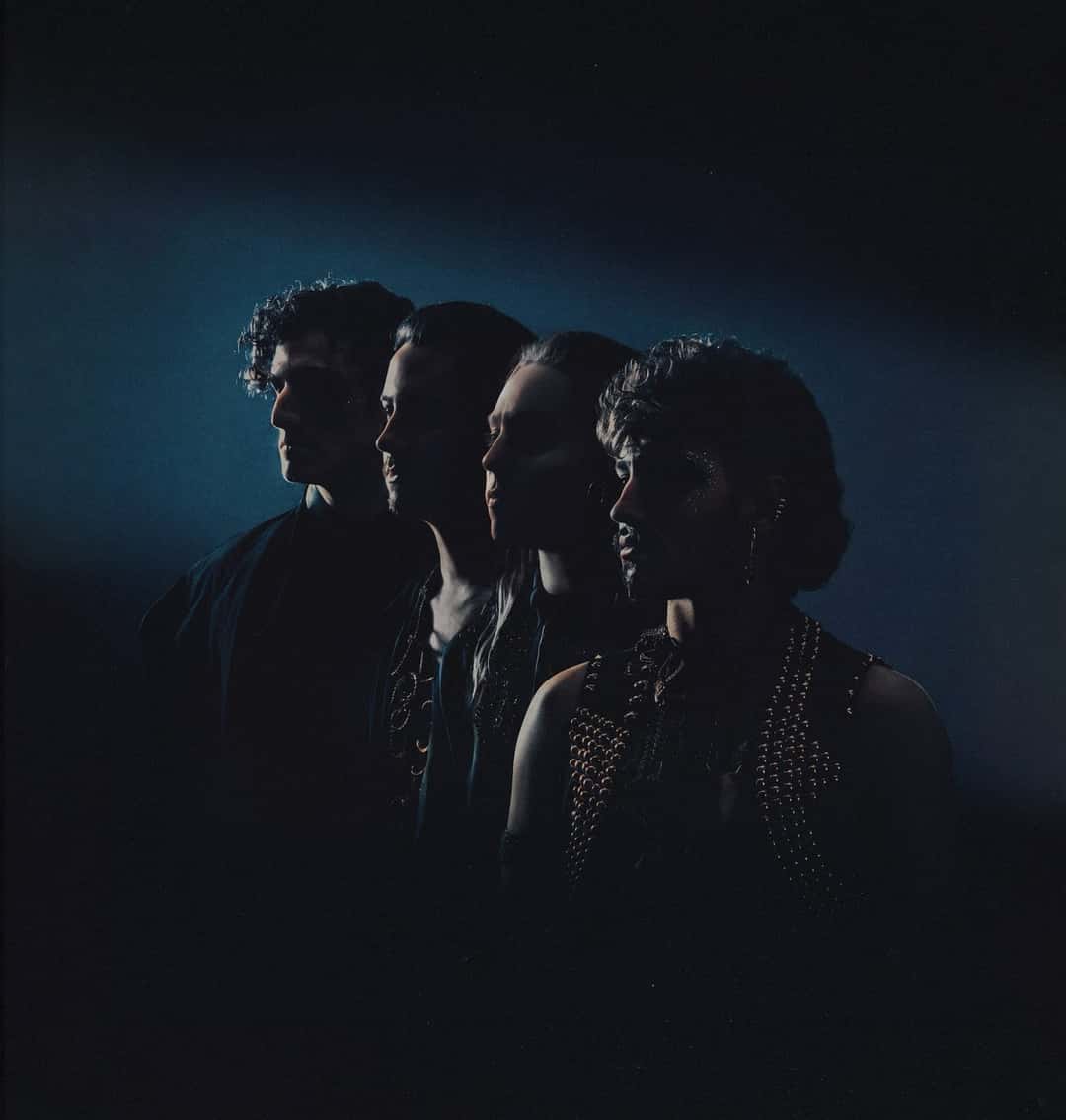Los cuatro integrantes de Greta Van Fleet de perfil, en fila y casi en silueta, iluminados por una luz azul sobre fondo negro