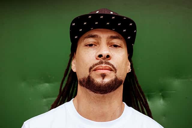 Roni Size en una foto de prensa de archivo: primer plano con gorra negra con estampado de estrellas y remera blanca, frente a una pared verde
