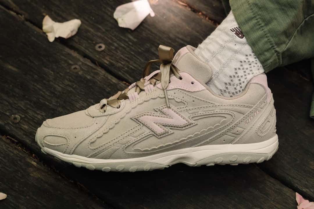 New Balance 740 del Sakura Pack en tono crema con la N rosa y cordones tipo cinta, sobre un piso de madera con pétalos