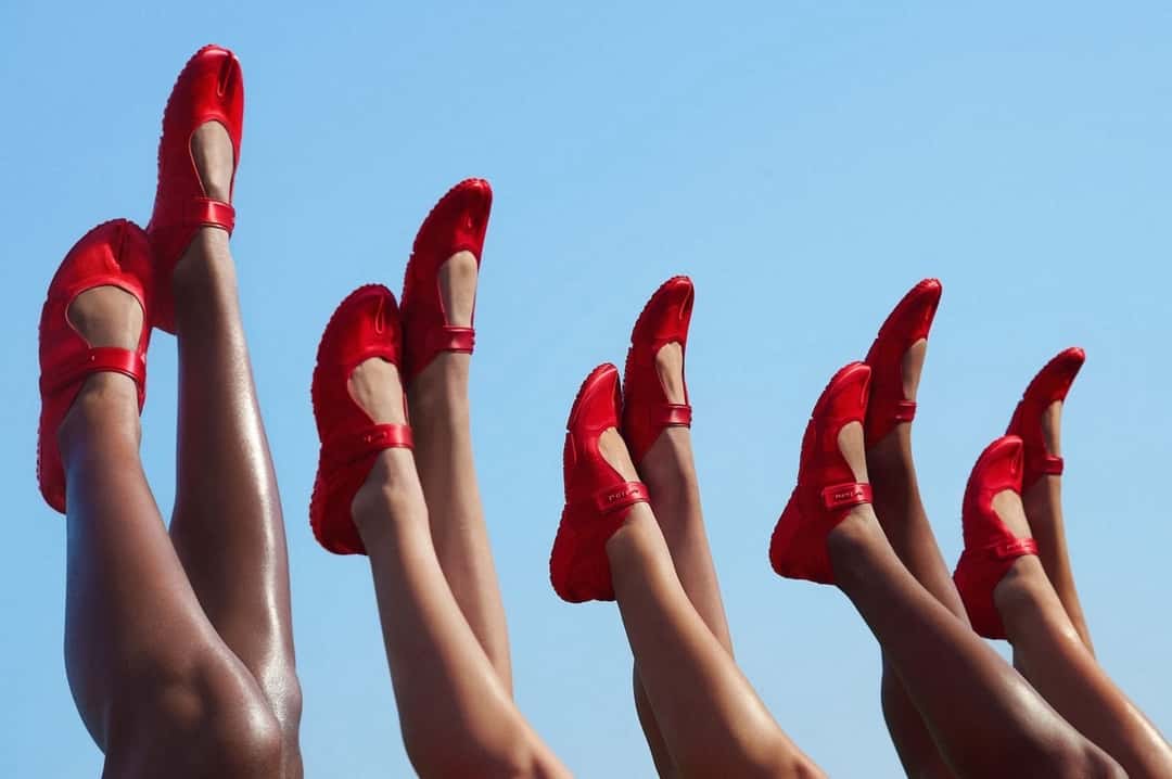 Piernas de porristas en el aire contra un cielo celeste, todas con la NikeSKIMS Rift Satin University Red, en una foto de la campaña de The Varsity Collection