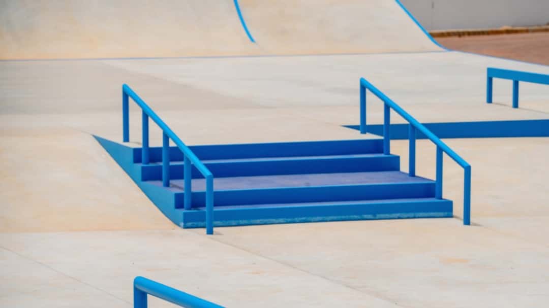 Una escalera de cuatro escalones con dos barandas, todo pintado de azul, en el skatepark de Dakar 2026, con rampas claras alrededor