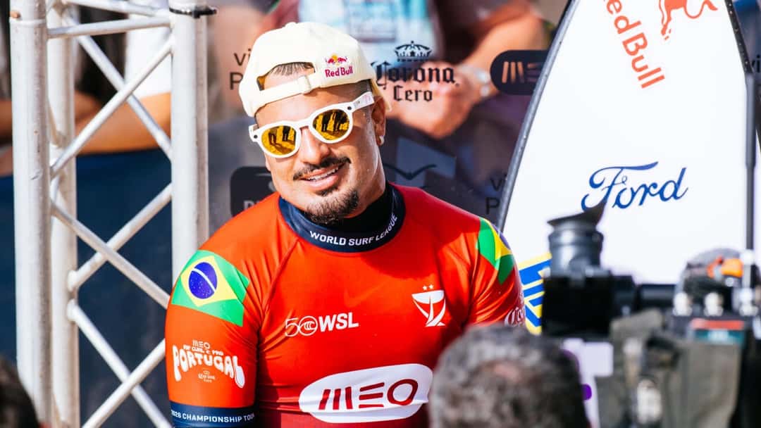 Ítalo Ferreira, con gorra blanca, anteojos de sol y la lycra roja del MEO Rip Curl Pro Portugal con la bandera de Brasil, sonríe en la zona de competidores de Supertubos