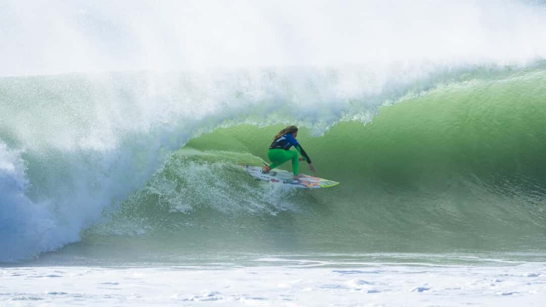 Erin Brooks, con lycra azul y calza verde, se mete en el tubo de una ola verde en Supertubos durante la primera ronda