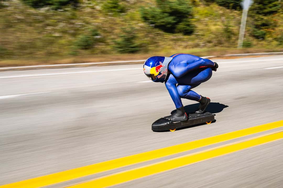 Diego Poncelet baja agachado sobre su skate con carenado negro, casco de Red Bull y traje aerodinámico azul, en una ruta de Quebec