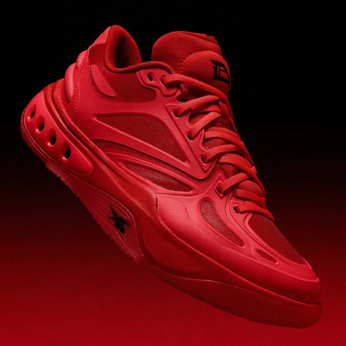 Reebok Engine A de Darius Acuff Jr. roja sobre fondo negro y rojo, con el logo DA en la lengüeta y el vector de Reebok en negro