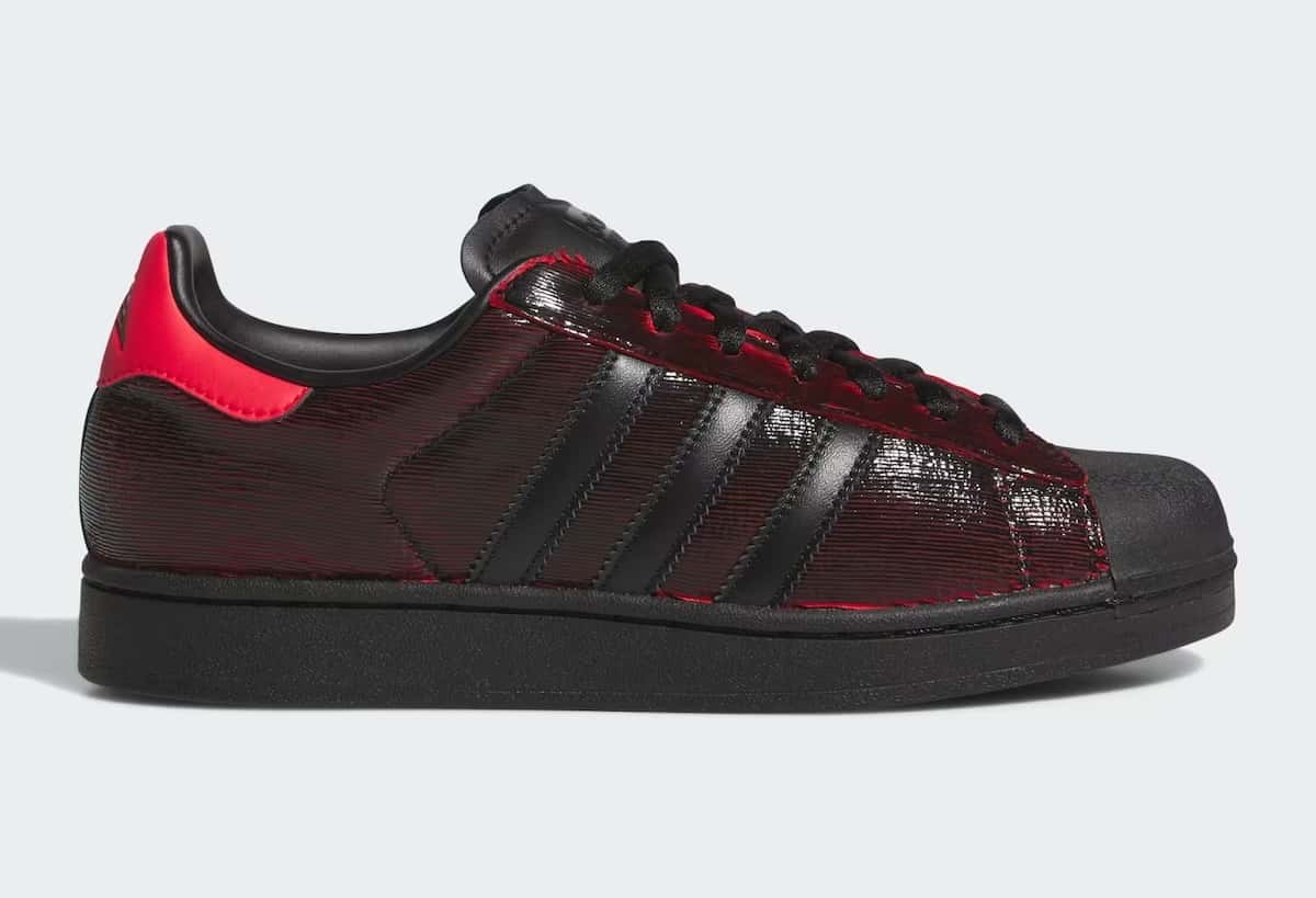 adidas Superstar Halloween de Anthony Edwards de perfil sobre fondo gris claro, con capellada negra y rayada que deja ver el rojo, talón rojo y suela negra