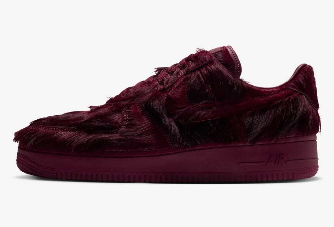 Nike Air Force 1 Low Pony Hair Team Red de perfil sobre fondo gris claro, con el pelo largo bordó tapando el Swoosh y los paneles, y la palabra Air en relieve sobre la mediasuela del mismo color