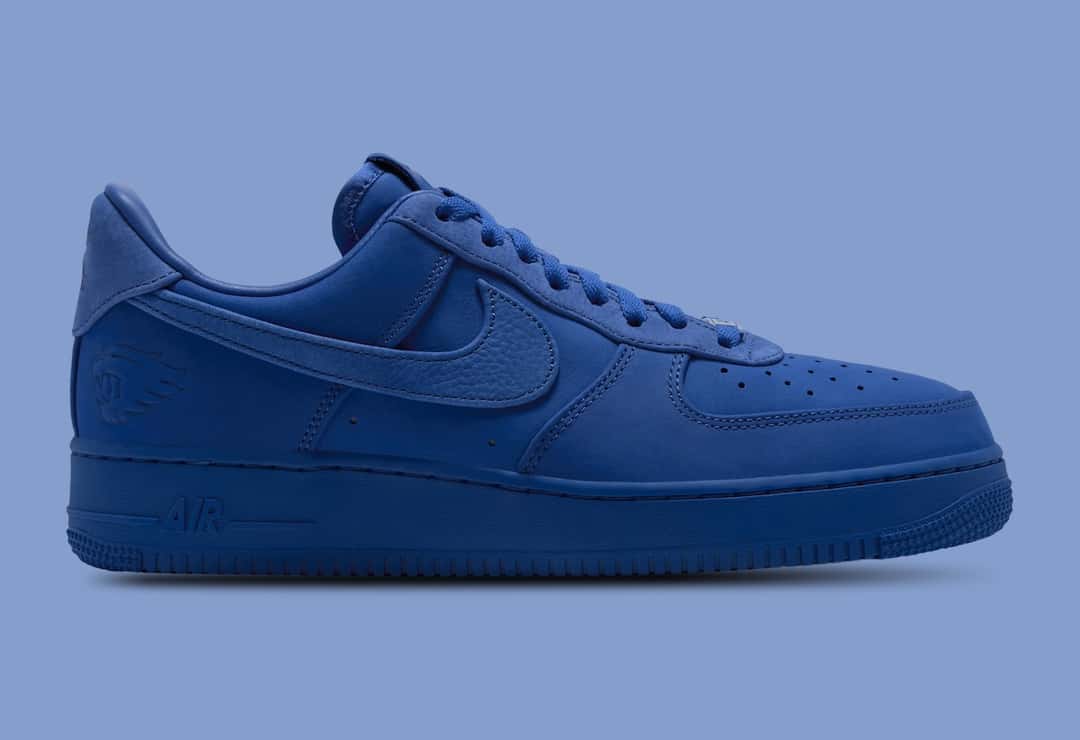 Nike Air Force 1 Low Luxe de la Universidad de Kentucky de perfil lateral sobre fondo celeste grisáceo, entero en azul rey, con el Swoosh de textura granulada y la cabeza del gato salvaje de Kentucky grabada en el talón