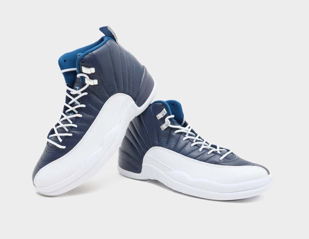 Par de Air Jordan 12 Obsidian apoyados uno junto al otro sobre fondo gris claro, con el cuero azul marino, la puntera blanca texturada y el forro azul en el cuello