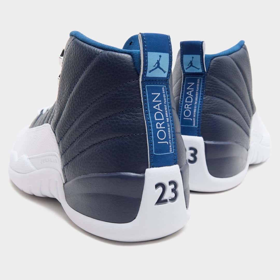 Vista trasera del par de Air Jordan 12 Obsidian, con el número 23 azul marino sobre el talón blanco y la tira azul con el logo Jordan y el Jumpman celeste