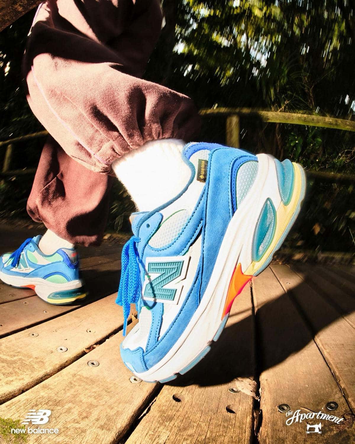 New Balance 2010 GORE-TEX Kingfisher de The Apartment en el pie, con gamuza azul, base verde agua y suela de colores, sobre un puente de madera