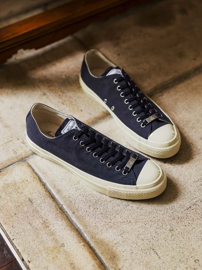 Brooks Brothers x Converse All Star Aged Ox en azul marino, apoyadas sobre baldosas claras, con suela y puntera color crudo, ojalillos plateados y la plaquita metálica en los cordones