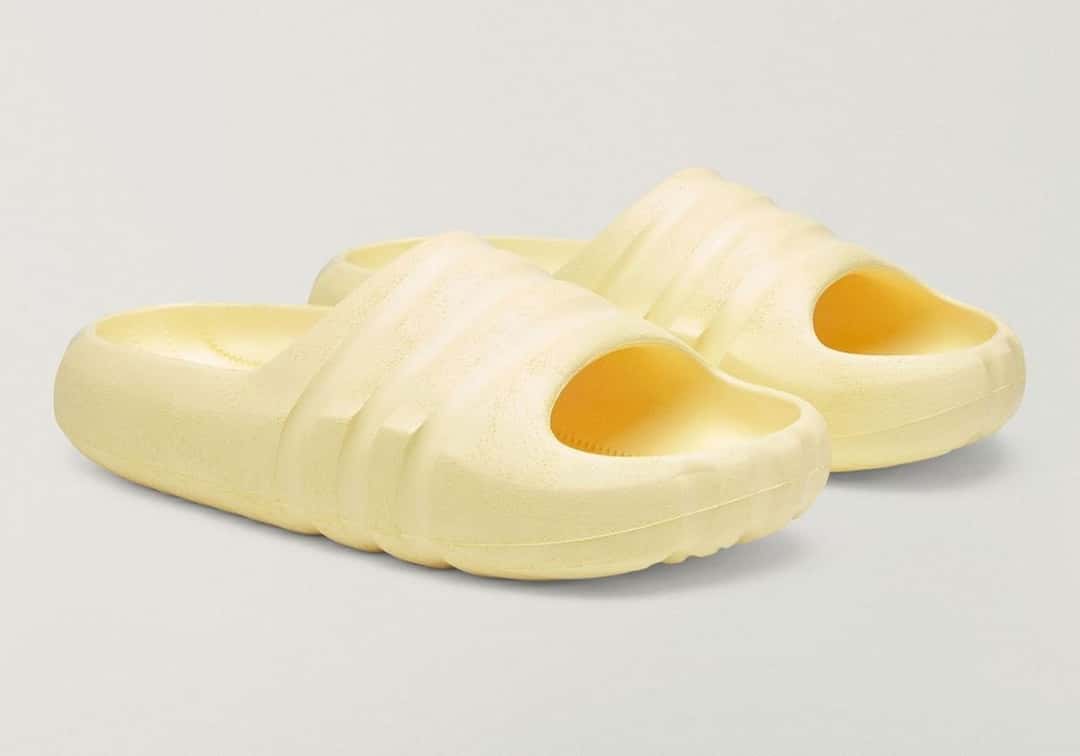 Ojota Bad Bunny x adidas BadBo Stone Slides amarilla de perfil, con la superficie rugosa y las tres franjas talladas
