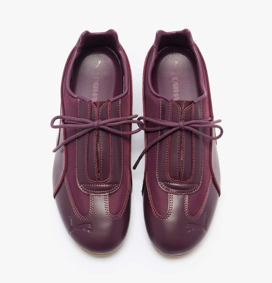 Vista superior del par PUMA Speedcat Slip-On de Daniëlle Cathari en cuero bordó, con paneles superpuestos, abertura central en el empeine, cordón fino atado en moño, Cat de PUMA grabado en la punta y la marca Cathari en la plantilla