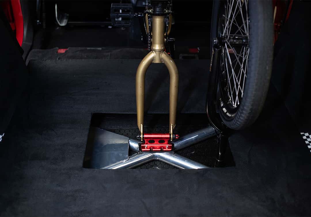 Soporte para la bici de BMX montado en la parte trasera del Acura ADX CZ-77, con la horquilla dorada fijada en una pieza roja