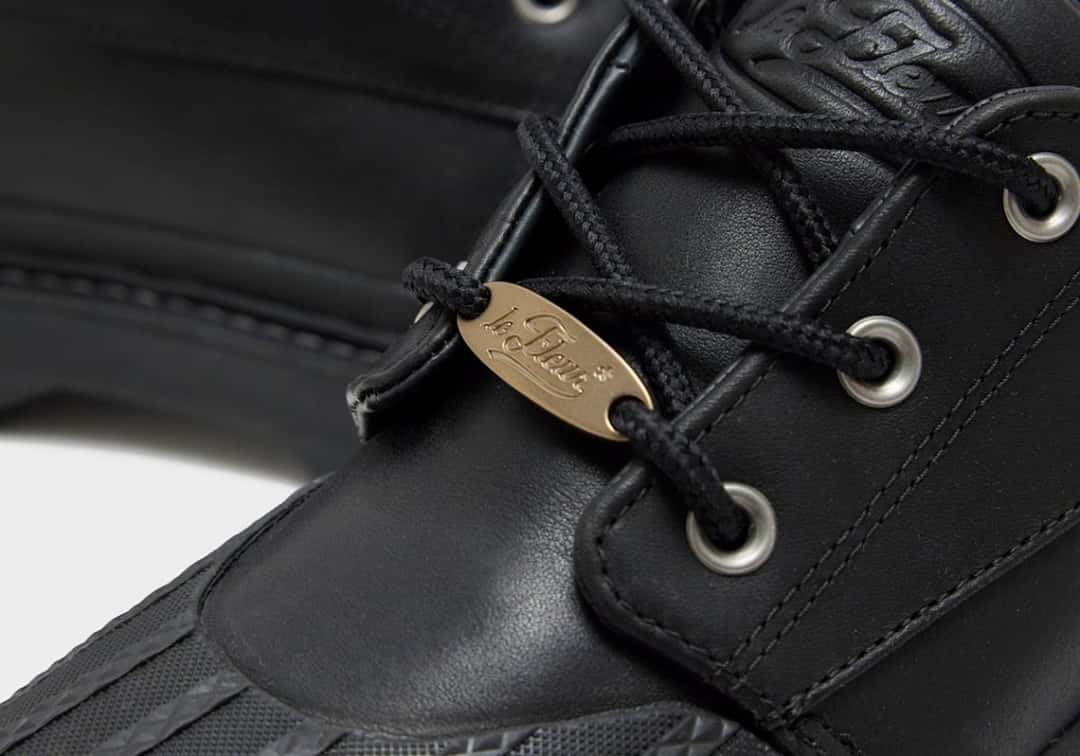 Primer plano del Converse 1908 Bronco Boot Low negro con la plaqueta dorada le FLEUR en los cordones, los ojales metálicos y el logo grabado en la lengüeta