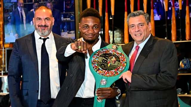 Christian Mbilli posa con el cinturón verde del Consejo Mundial de Boxeo, junto a dos dirigentes de traje