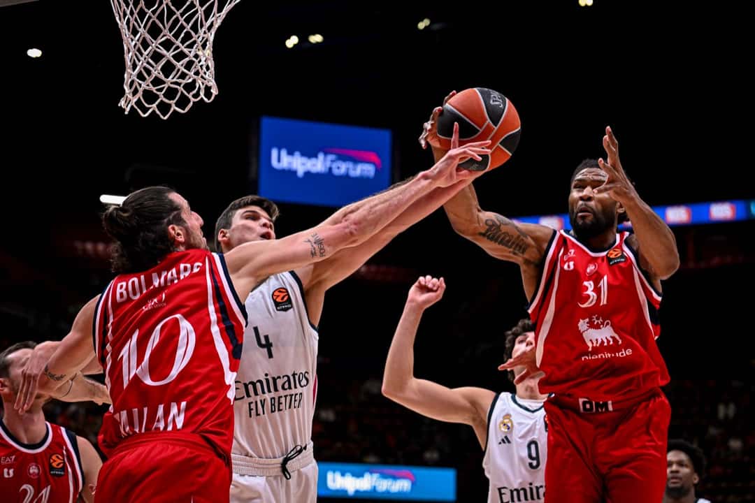 Leandro Bolmaro, con la camiseta roja número 10 del Olimpia Milano, pelea la pelota con un jugador del Real Madrid de camiseta blanca, debajo del aro del Unipol Forum