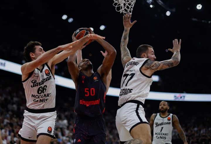 Jugadores del Partizan, con camiseta blanca, defienden bajo el aro a un jugador del Bayern Múnich de camiseta oscura con el número 50, en el SAP Garden de Múnich