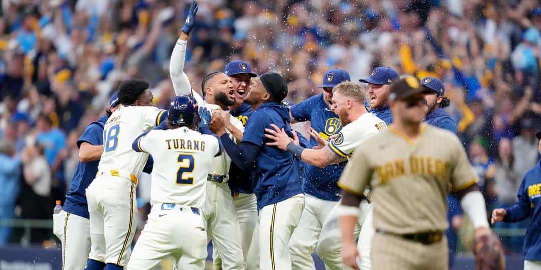 Los jugadores de los Brewers festejan en el campo de American Family Field después del sencillo ganador de Jackson Chourio, mientras un jugador de los Padres camina de espaldas a la celebración