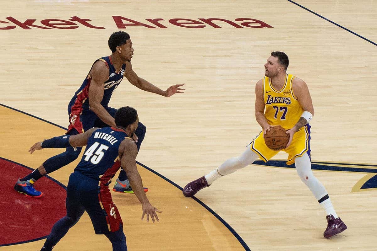 Foto de archivo: Luka Doncic, con la camiseta amarilla número 77 de los Lakers, sostiene la pelota frente a dos defensores de Cleveland