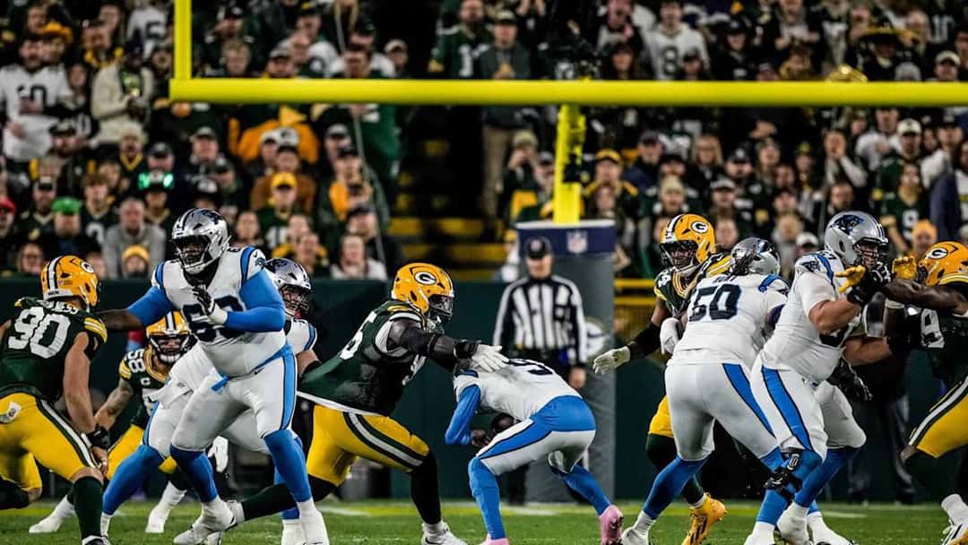 La línea de los Packers, de verde, y la de los Panthers, de blanco, chocan en la línea de golpeo frente a los postes, con la tribuna llena del Lambeau Field detrás