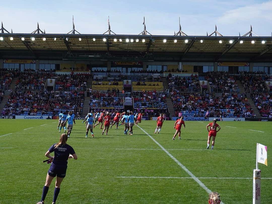 Foto de archivo: jugadoras de Gales, de rojo, y de Fiyi, de celeste, en la cancha durante un partido del Mundial femenino 2025, con las tribunas llenas