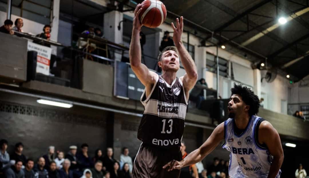 Un jugador de Oberá, con la camiseta blanca número 1, defiende el lanzamiento de un jugador de Platense, de marrón, en una cancha con público