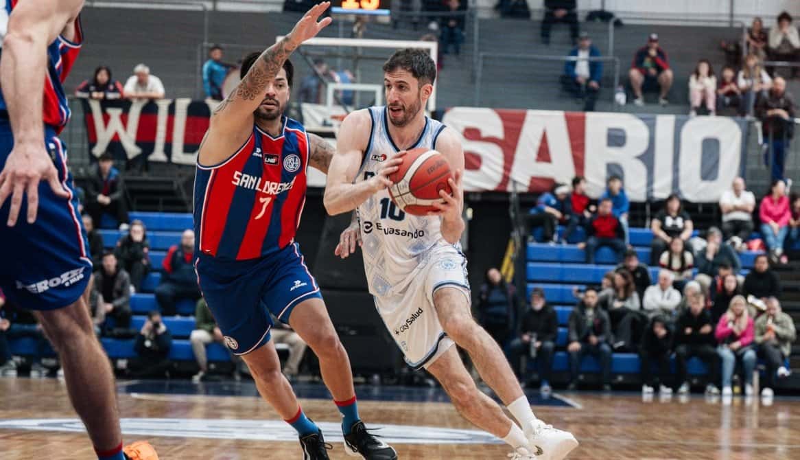 Un jugador de Oberá, con la camiseta blanca número 10, avanza con la pelota ante la marca de un jugador de San Lorenzo, de azul y rojo