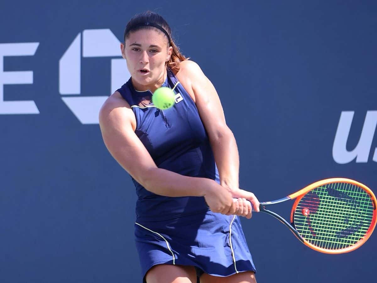 Foto de archivo: Julia Riera, con vestido azul oscuro y vincha, le pega un revés a dos manos frente a un cartel del US Open 2023