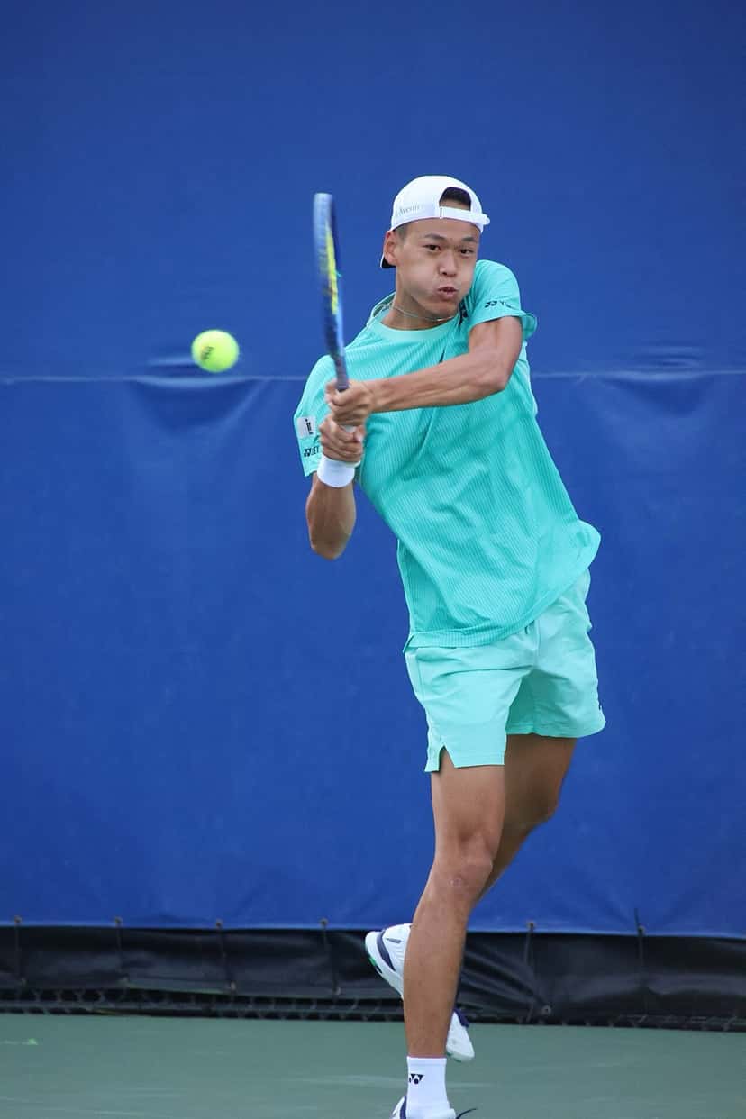 Foto de archivo: Rei Sakamoto, con gorra blanca y conjunto verde agua, pega un revés a dos manos frente a una lona azul, en un partido de 2026 en Cary, Estados Unidos