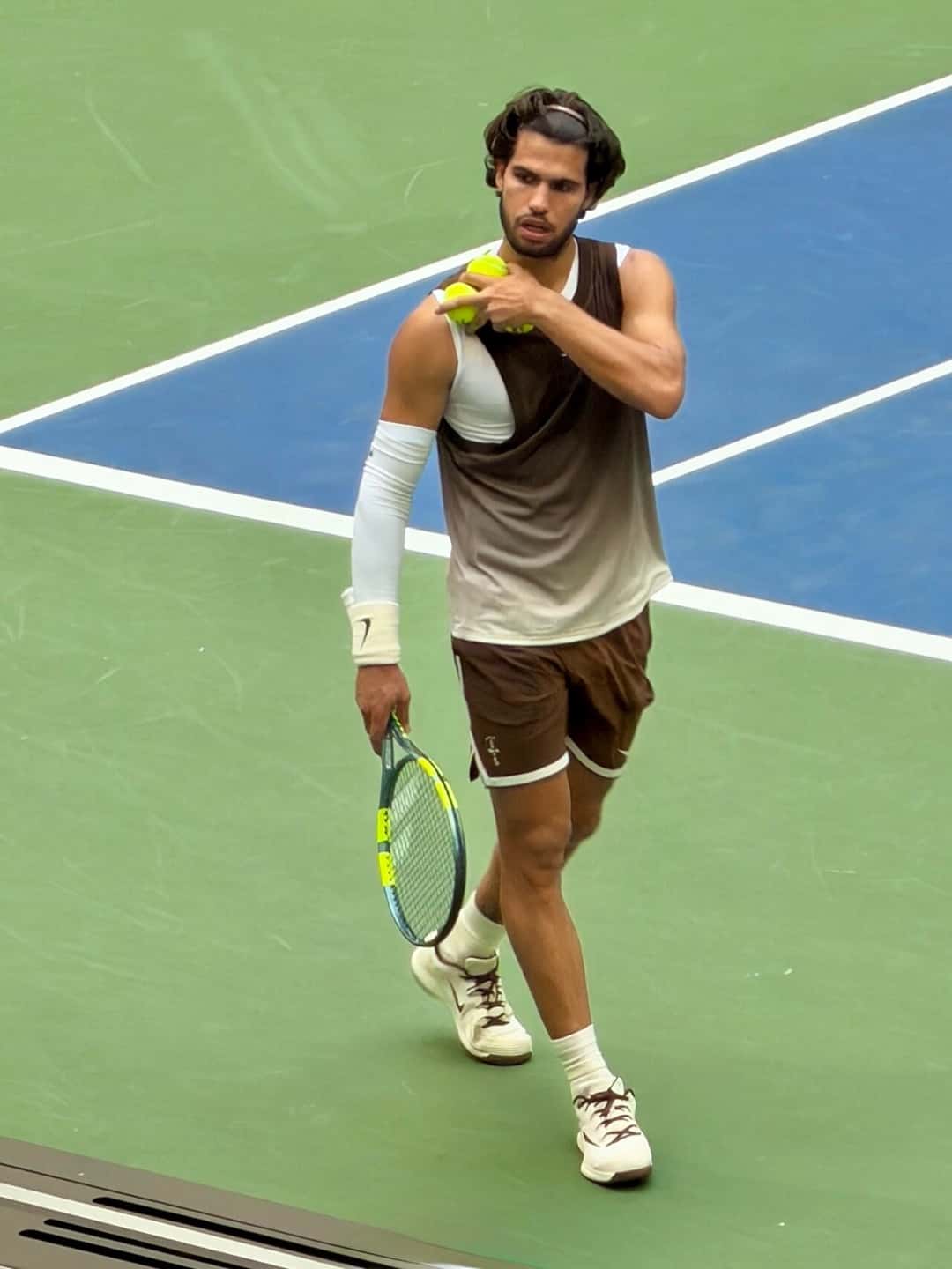 Foto de archivo: Carlos Alcaraz, con musculosa marrón y blanca, camina por la cancha con pelotas en la mano en el US Open 2026