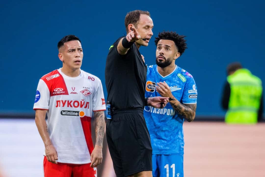 Esequiel Barco, con la camiseta blanca y roja de Spartak de Moscú, junto al árbitro y a un jugador de Zenit en el Gazprom Arena de San Petersburgo. Foto de archivo de agosto de 2024, publicada por el sitio oficial de Zenit (fotógrafo: Viacheslav Evdokimov, licencia CC BY-SA 3.0, vía Wikimedia Commons)