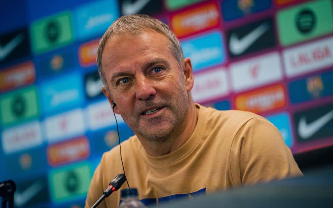 Hansi Flick, entrenador del Barcelona, sonríe en la conferencia de prensa previa al partido con el Betis, con un panel de patrocinadores de fondo (foto: FC Barcelona)