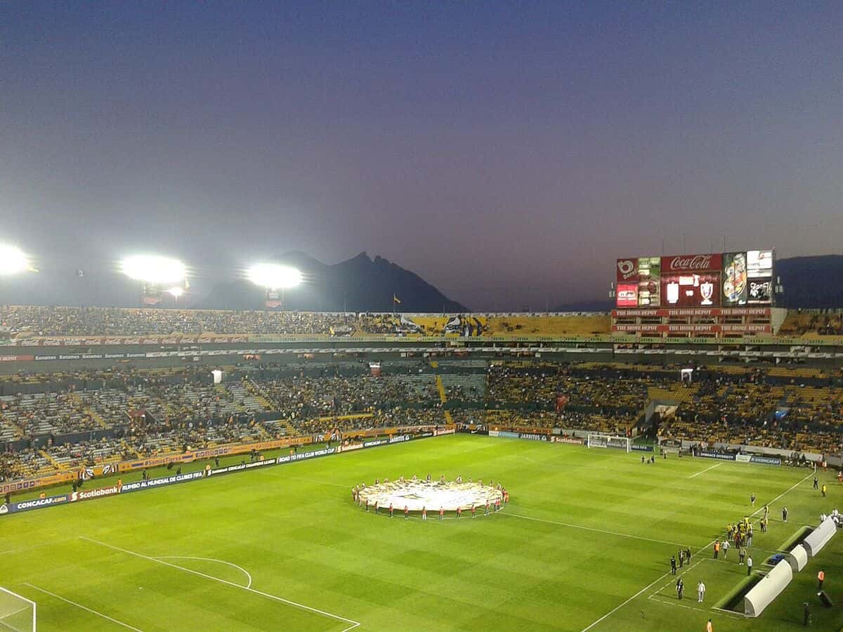 El estadio Universitario de Tigres, en San Nicolás de los Garza, de noche, con las tribunas llenas de hinchas de amarillo y los cerros de Monterrey de fondo; foto de archivo de 2016 (foto: J4im31000, Wikimedia Commons, dominio público)