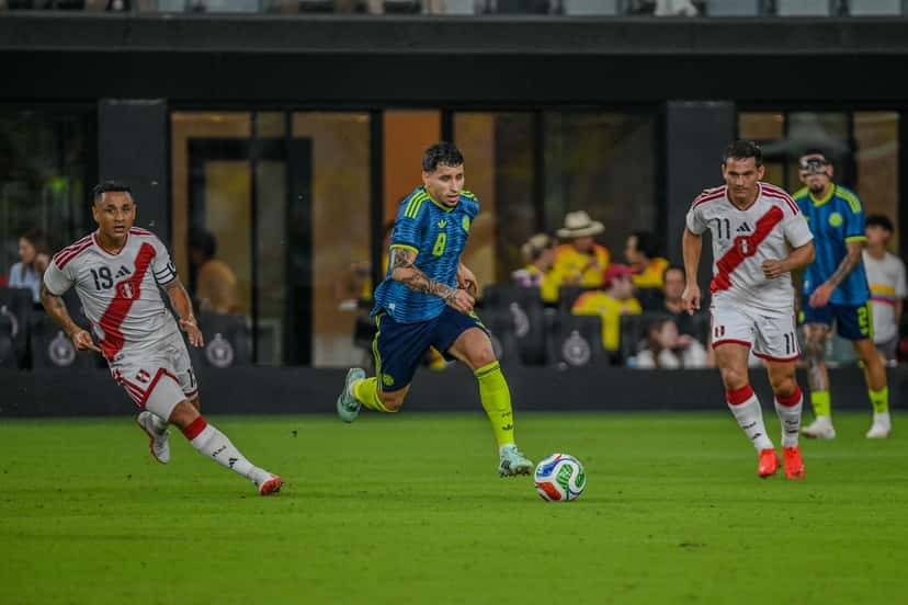 Un mediocampista de Colombia con la camiseta 8 conduce la pelota entre dos jugadores de Perú, de camiseta blanca con la franja roja, en el Nu Stadium de Miami (foto: prensa oficial de la Federación Colombiana de Fútbol)