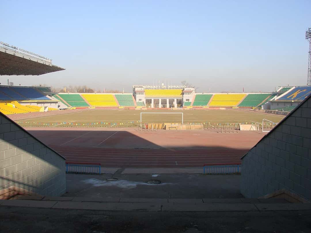 Las tribunas vacías del estadio Central de Almaty, con butacas amarillas, verdes y azules alrededor de la cancha y la pista de atletismo; foto de archivo de 2008 (foto: Дмитрий Никишин, Wikimedia Commons, dominio público)
