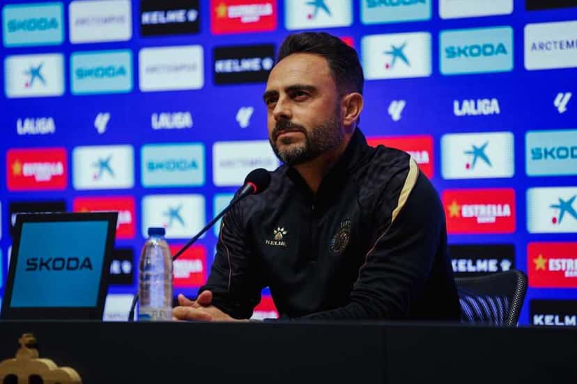 Sergio García, entrenador interino del Espanyol, con campera negra, habla en la conferencia de prensa previa al partido con el Villarreal, frente al panel de sponsors del club (foto: prensa RCD Espanyol)