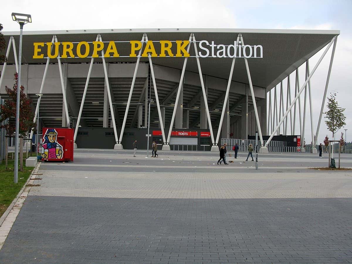 La entrada del Europa-Park Stadion de Friburgo, con su techo blanco sostenido por columnas inclinadas y el nombre del estadio en letras amarillas; foto de archivo de octubre de 2021 (foto: Andreas Schwarzkopf, Wikimedia Commons, licencia CC BY-SA 4.0)