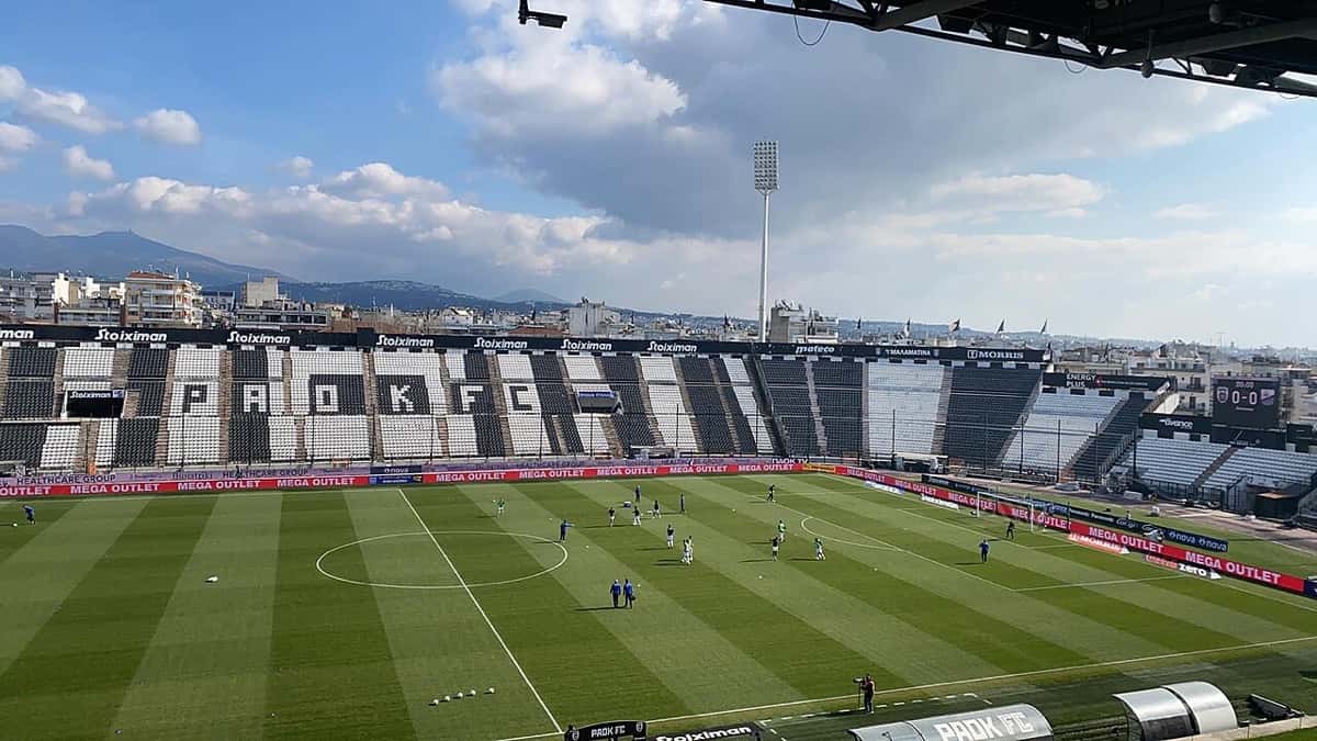 Vista del Toumba de Salónica, el estadio del PAOK, con las tribunas vacías y los jugadores haciendo la entrada en calor (foto de archivo: Αθλητικά, Wikimedia Commons, CC BY-SA 4.0)