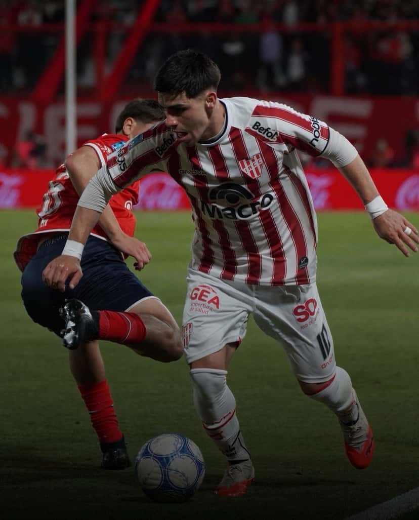 Un jugador de Instituto, con la camiseta blanca y roja a bastones, conduce la pelota ante la marca de un futbolista de Independiente en Avellaneda